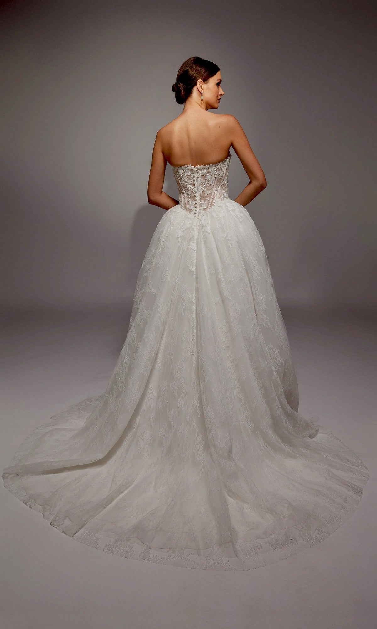 A woman faces away from the camera, wearing the Long White Dress: Alyce 7163—an ivory ball gown wedding dress with a strapless lace design, corset bodice, and elegant long train.